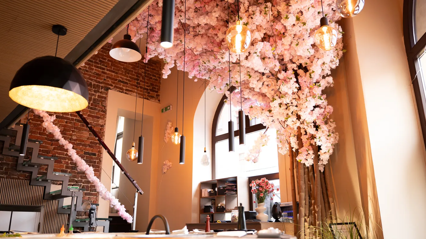 Wnętrze Sakura Sushi Bar — baldachim kwitnącej sakury nad barem, ceglana ściana i ciepłe światło